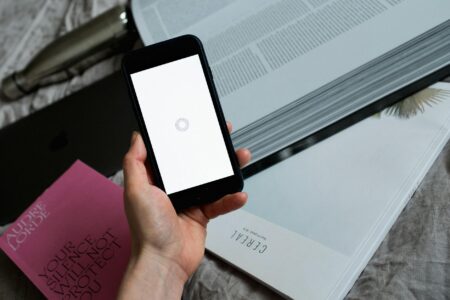 Person holding smartphone while reading books, representing social media book culture