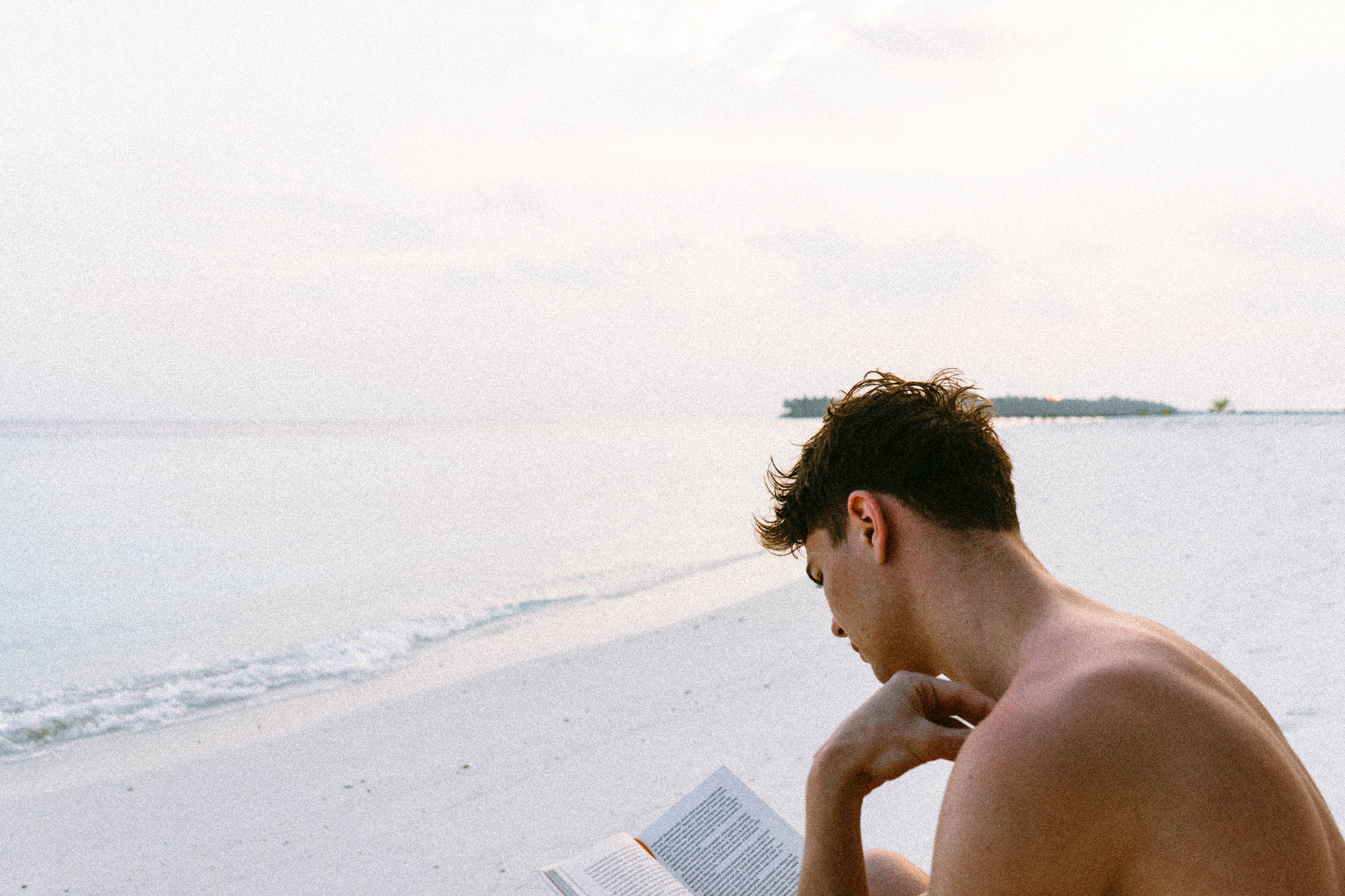 Person reading a book on a sunny beach with sunglasses resting on the cover