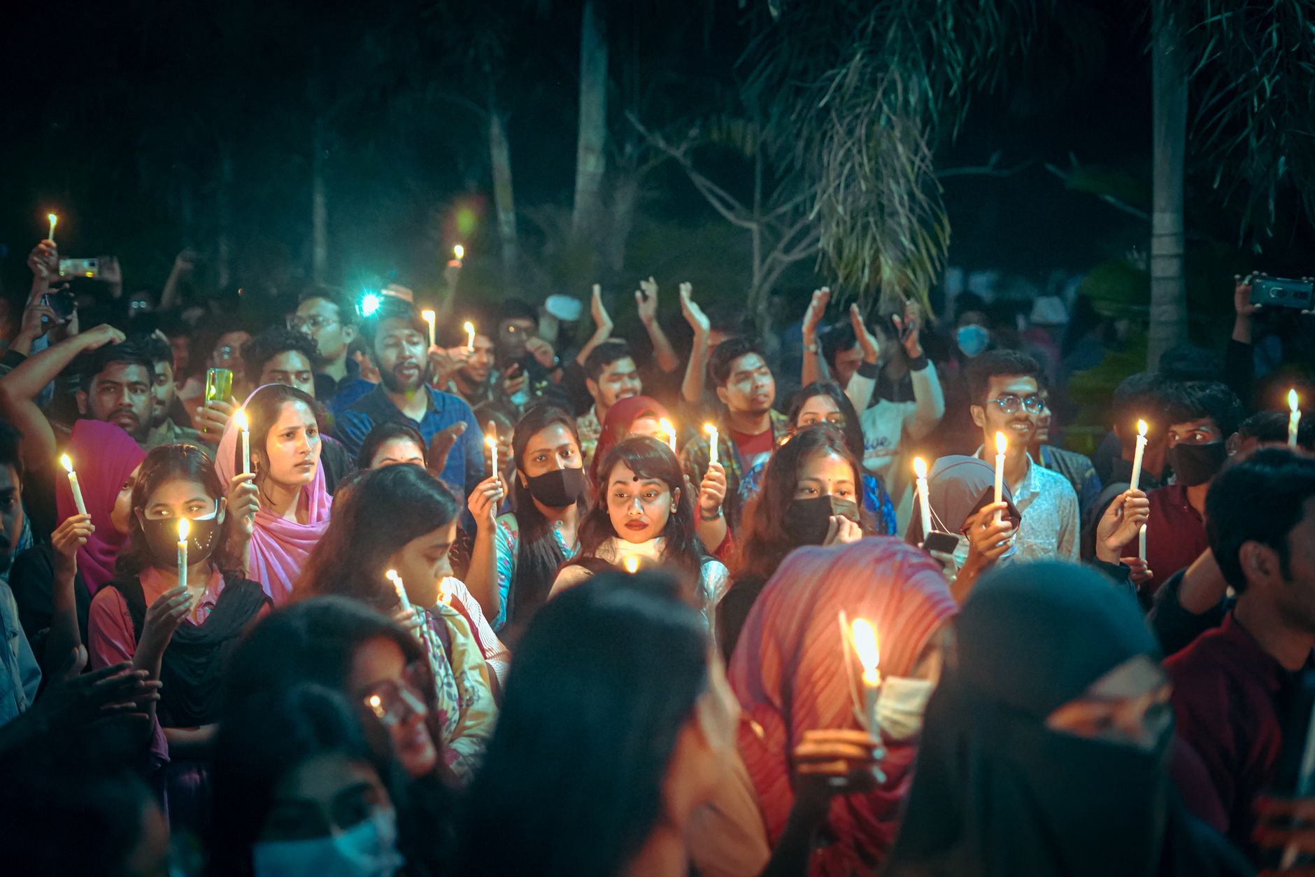People holding candles at a public vigil in an outdoor setting