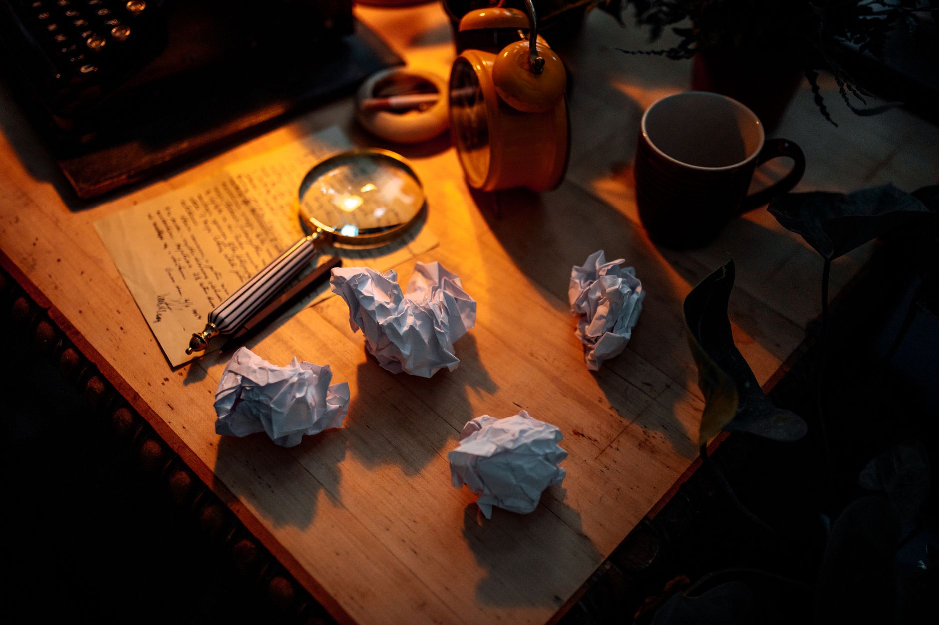 A writer's desk lit by a single lamp at night, manuscript pages visible