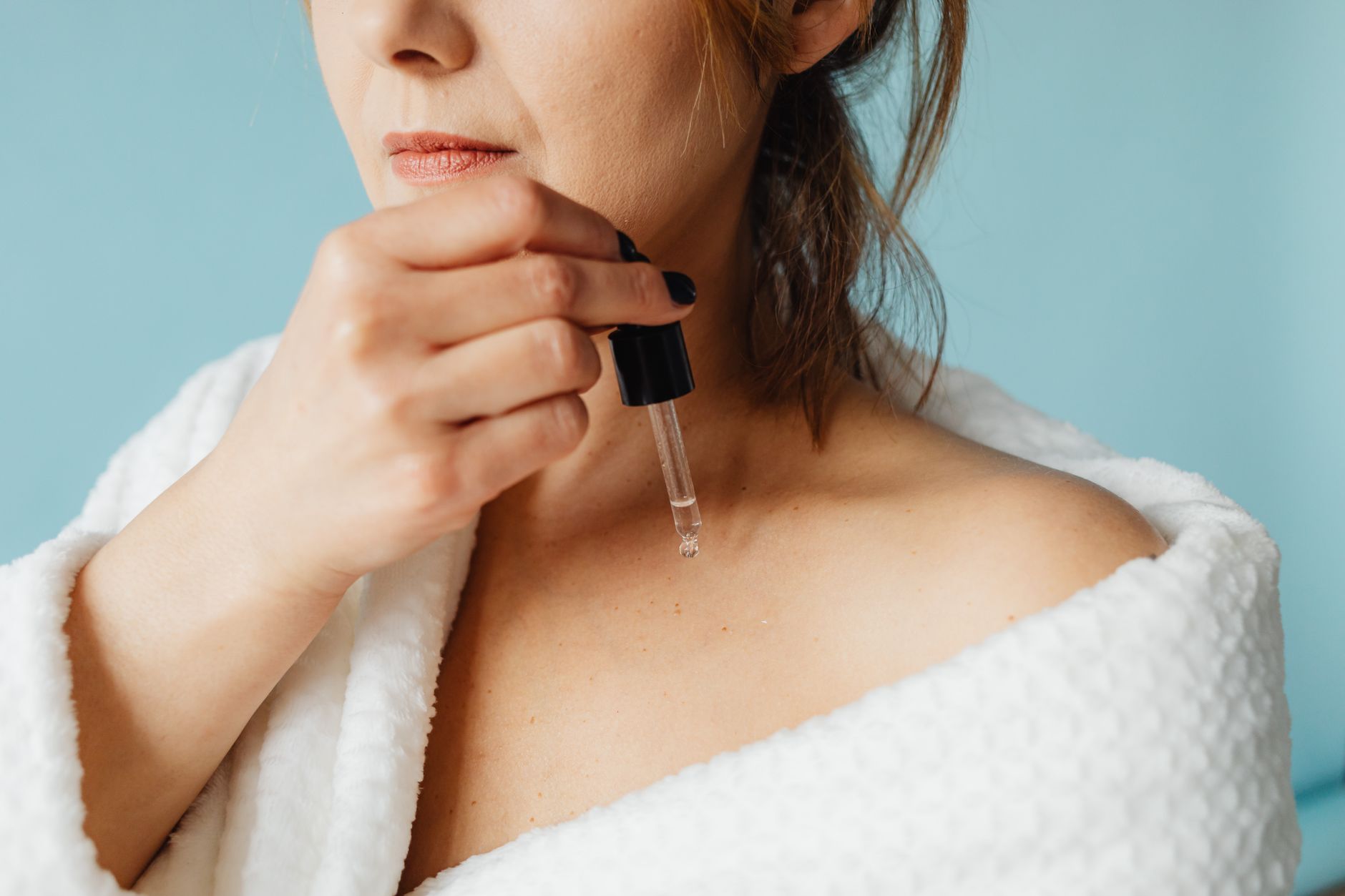 Close-up of a serum dropper bottle with liquid droplet, representing layered skincare application