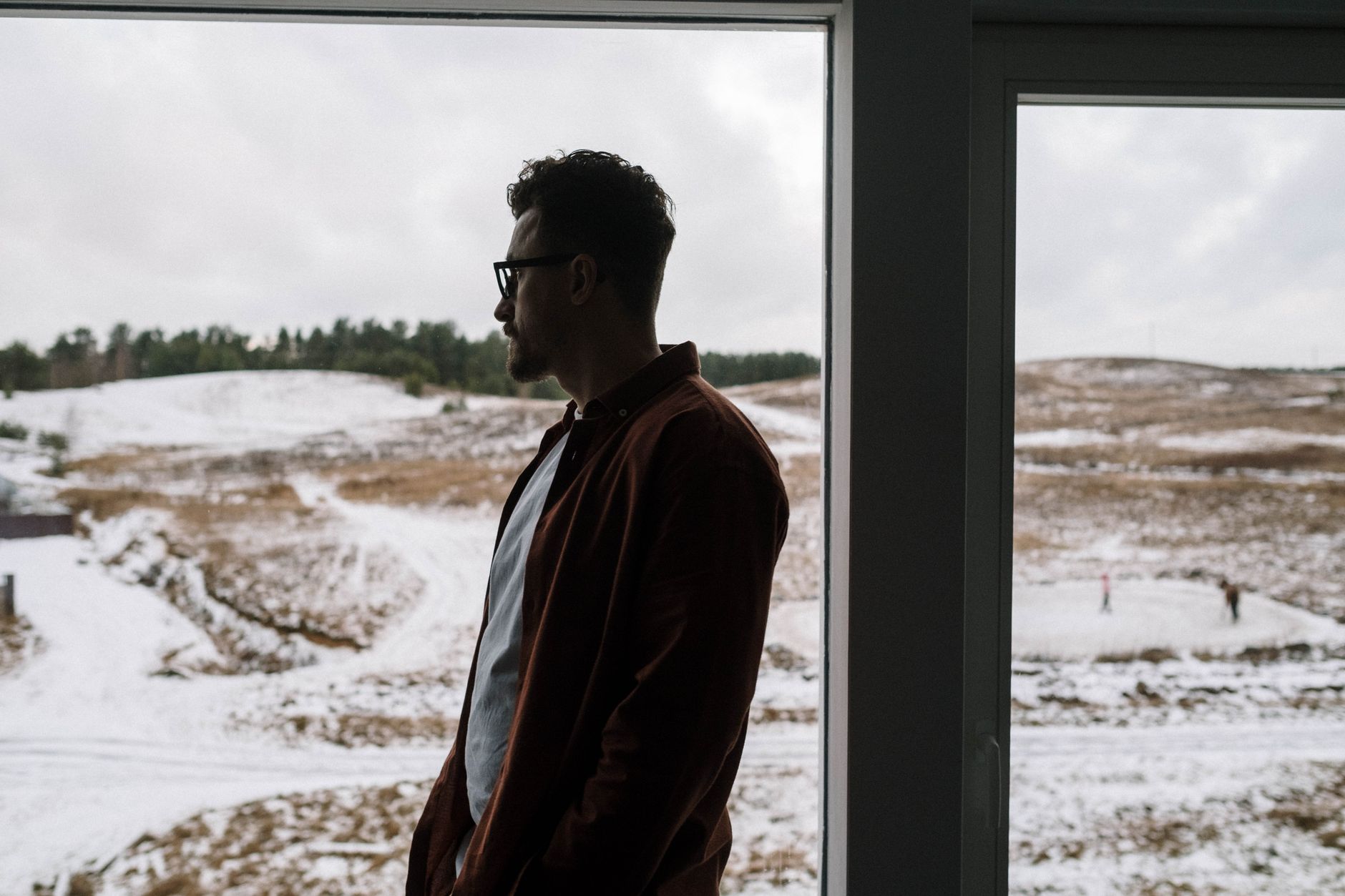 A person sitting alone near a frost-covered window in winter, looking out in quiet grief