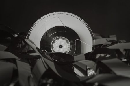 A stack of literary novels next to a vintage film reel on a wooden surface