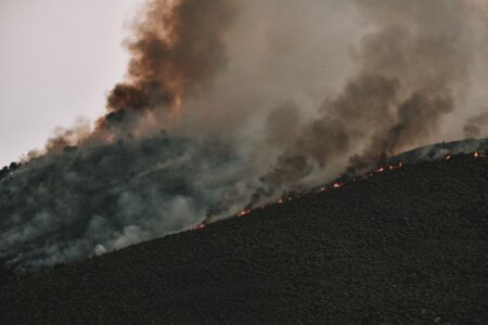 Smoke and flames rising over dry hillside terrain during an active wildfire