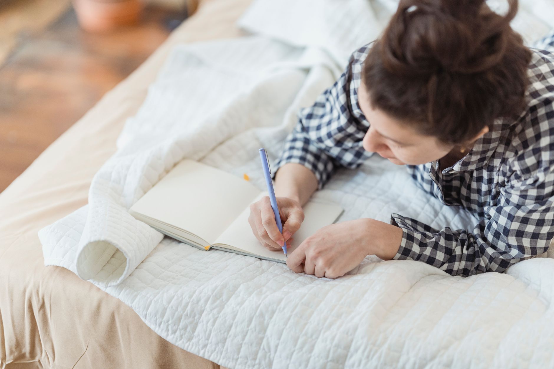 A person writing by hand in a journal at a wooden desk, natural light coming from a window