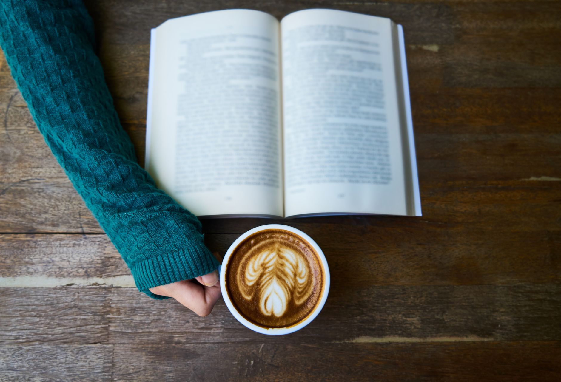 Person reading a book alone at a small cafe table with a coffee cup nearby
