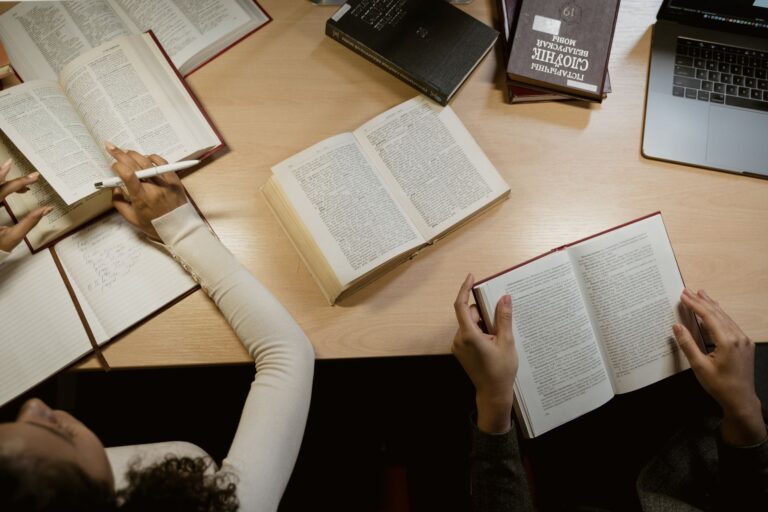 Stack of open books on a wooden reading desk with natural light