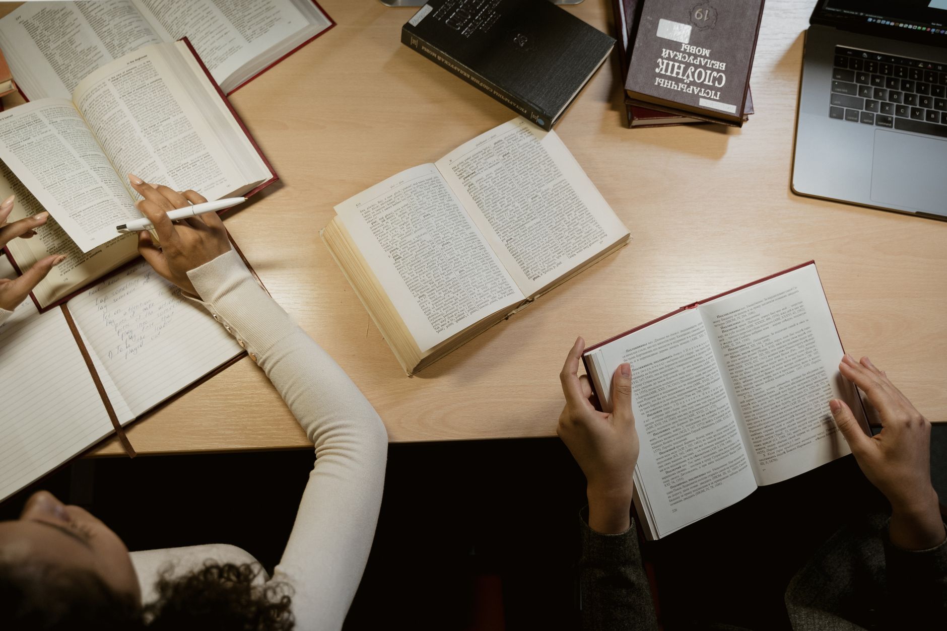 Stack of open books on a wooden reading desk with natural light