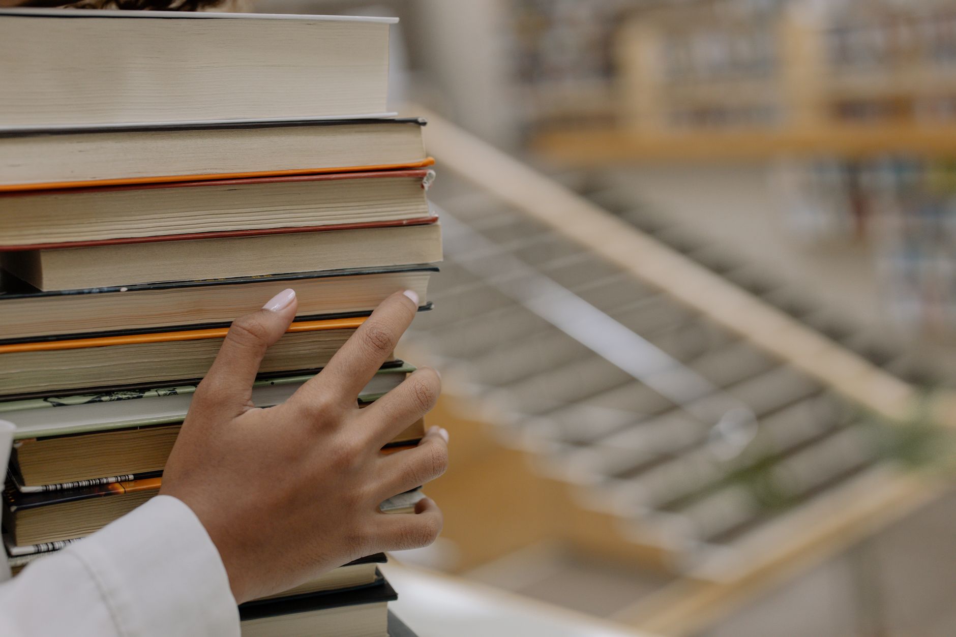 A tall, uneven stack of hardcover and paperback books beside a reading lamp