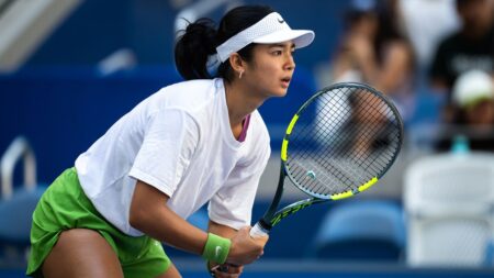 A young tennis player preparing to serve on a hard court during a major tournament