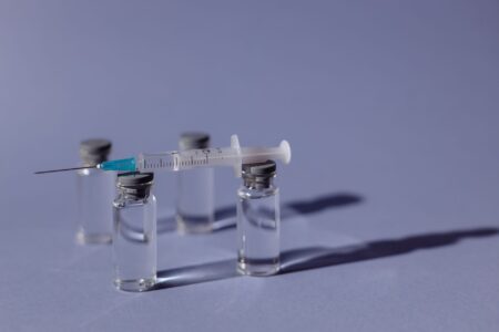 A COVID-19 vaccine vial and syringe on a medical surface