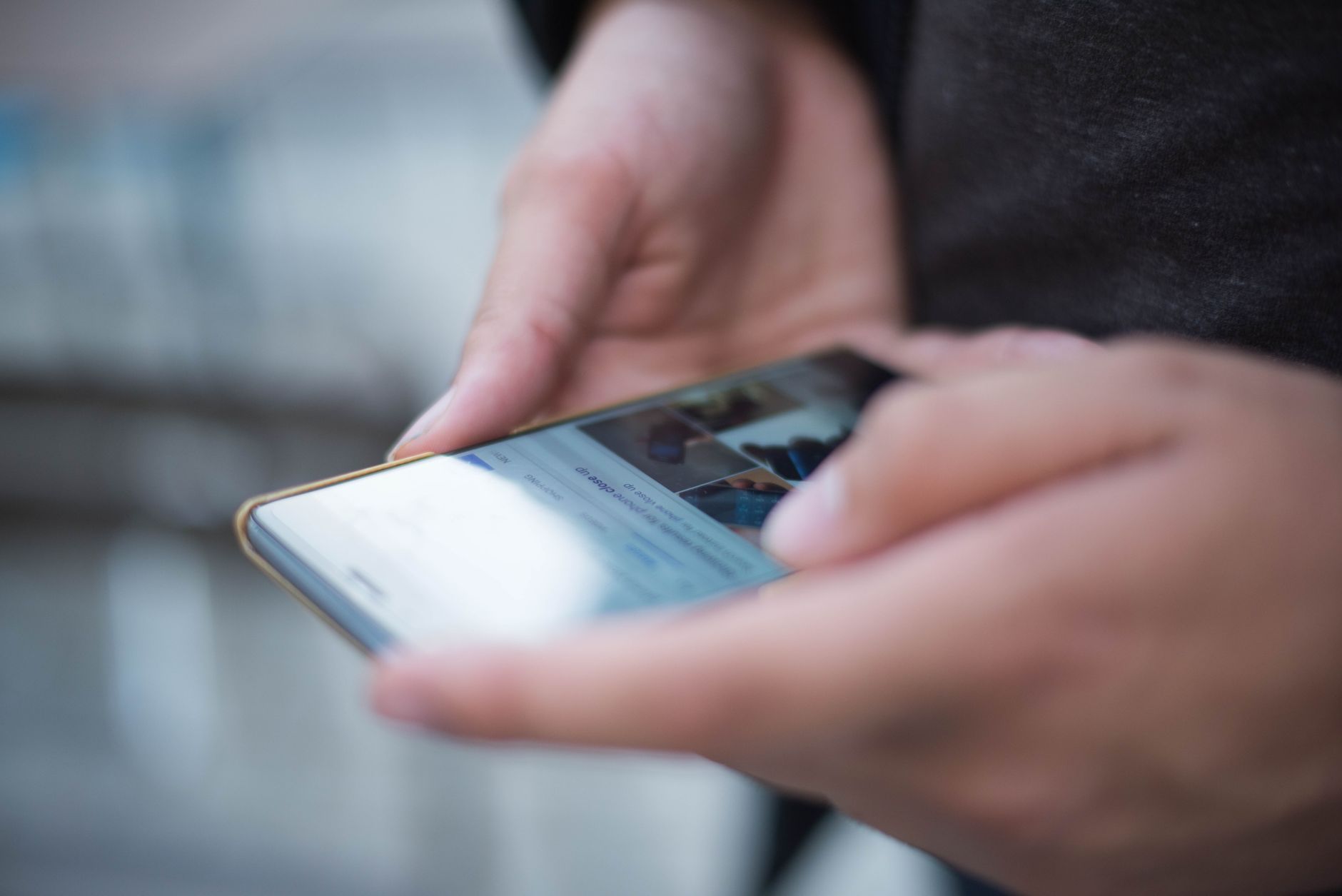 Close-up of hands holding a smartphone, screen lit with a social media feed